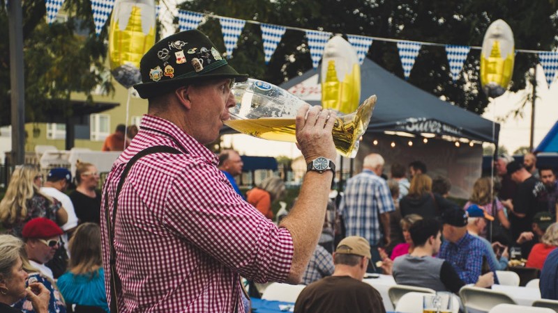 Man enjoying a large beer mug at an Oktoberfest celebration outdoors with a lively crowd., tags: die - pexel